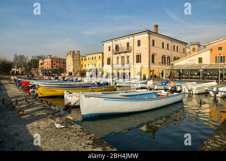 View of the port of the old town on the shore of Lake Garda, with docked boats, the town hall and the medieval tower, Bardolino, Verona, Veneto, Italy Stock Photo