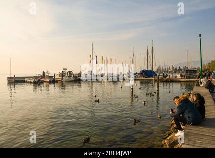 Scenic view of the lakeside promenade of Bardolino with people sitting on the shore of Lake Garda and the harbor in the background, Veneto, Italy Stock Photo