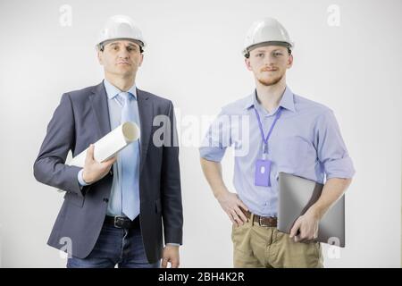 Two engineers confidently look at camera with smile, holding laptop and drawing Stock Photo