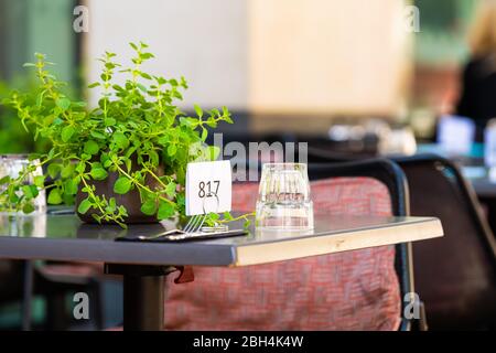 Closeup of glass cup upside down on restaurant table outside street cafe with order number sign and green plant in summer with nobody empty patio Stock Photo