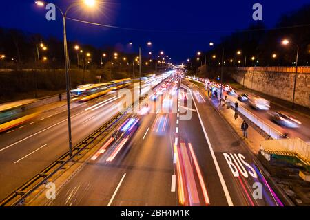 Long exposure above high angle aerial view of Aleja Armii Ludowej street in Warsaw, Poland at night with traffic cars, people standing at bus stop wit Stock Photo