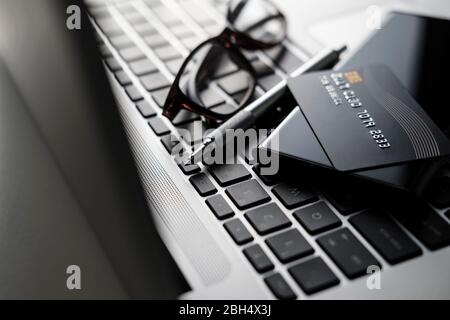 Credit card, smart phone, pen and glasses on laptop keyboard Stock Photo