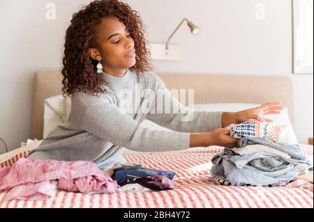 Woman sitting on bed folding clothes Stock Photo