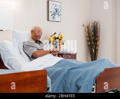 Senior man holding smart phone and flowers in bed Stock Photo