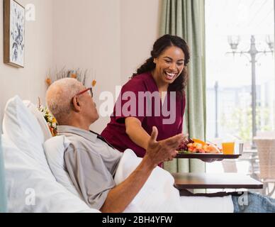 Smiling nurse hanging food to senior man in bed Stock Photo