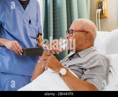 Senior man drinking water in bed Stock Photo