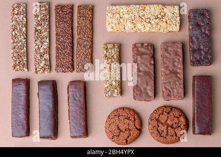 Different Energy protein bars and oatmeal bars on light brown chocolate background. Set of energy, sport, breakfast and protein bars. Copy space. Flat Stock Photo
