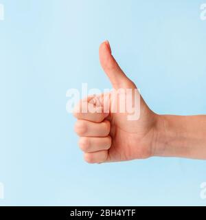 Closeup of female hand showing thumbs up sign against pastel blue background, copy space, minimal concept Stock Photo