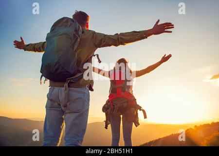 Couple with raised arms holding hands and looking at sunset Stock Photo