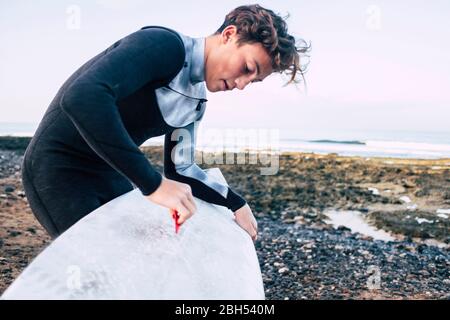 Teenage boy waxing surfboard at beach Stock Photo