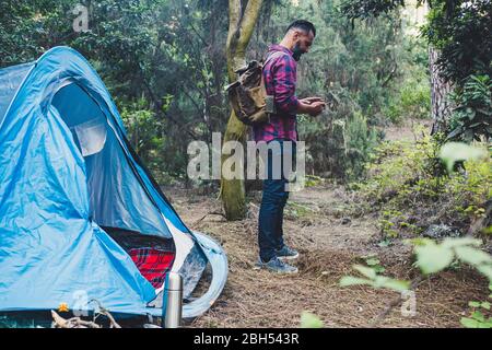 Man using smart phone by tent in forest Stock Photo