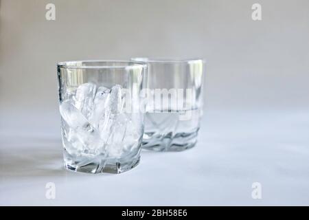 Profile view of drinking glasses of ice and water (melted ice) in transparent tumblers on a neutral background, concepts of time and change, color Stock Photo