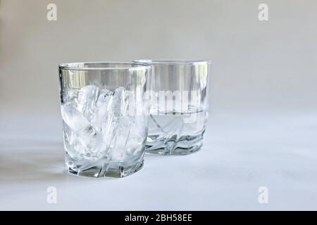 Profile view of drinking glasses of ice and water (melted ice) in transparent tumblers on a neutral background, concepts of time and change, color Stock Photo