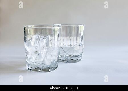 Profile view of drinking glasses of ice and water (melted ice) in transparent tumblers on a neutral background, concepts of time and change, color Stock Photo