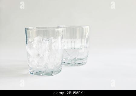 Profile view of drinking glasses of ice and water (melted ice) in transparent tumblers on a neutral background, concepts of time and change, color Stock Photo