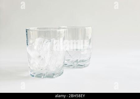 Profile view of drinking glasses of ice and water (melted ice) in transparent tumblers on a neutral background, concepts of time and change, color Stock Photo
