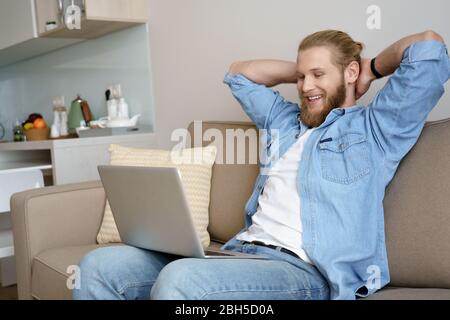 Happy young man relax on couch at home watching movie on laptop. Stock Photo