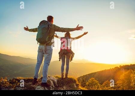 Couple with raised arms holding hands and looking at sunset Stock Photo