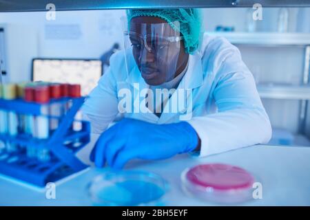 African doctor sitting at the table and examining medical samples in test tubes in medical lab Stock Photo