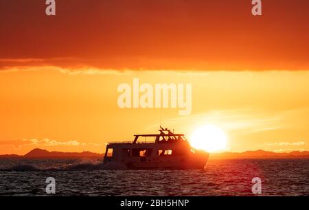 Boat sailing by the coast of Belize with sun setting down in the background and lighting up the sky Stock Photo