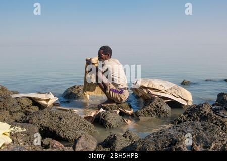 A man washes bags, recycling them, on the rocks at the shore of a lake near Addis Ababa. In Ethiopia, Africa. Stock Photo