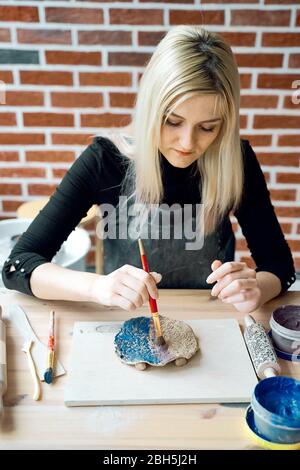 Woman making pattern on ceramic plate with paint brush. Creative hobby concept. Earn extra money, side hustle, turning hobbies into cash, passion into Stock Photo