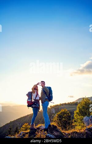 Hikers with backpacks relaxing on top of a mountain and enjoying the view of valley Stock Photo