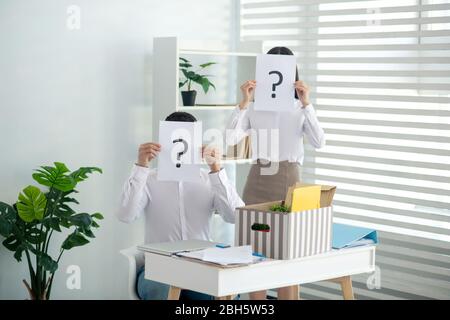 At work. Male and female colleagues holding papers with question marks Stock Photo