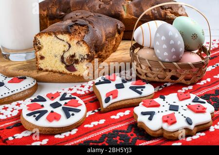 Slices of Romanian sponge cake with red traditional towel with manual stitch on wooden board, Easter painted eggs and home made ginger bread hearts, A Stock Photo