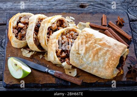 German traditional pastry apple strudel roll with caramelized apples, nuts, cinnamon, raisins served on a brown cutting board with star anise, cinnamo Stock Photo
