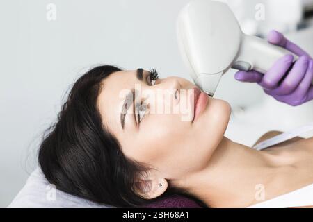 Pretty brunette woman getting hair removing on face. Procedure laser epilation at beauty studio Stock Photo