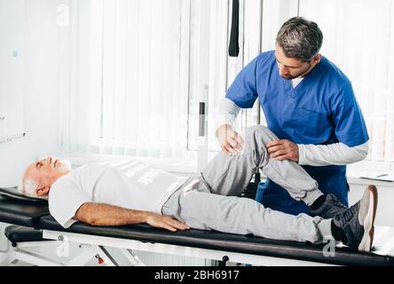 physiotherapist treating leg injury on a man lying down. Senior man training with his therapist. Joint, knee and leg pain treatment Stock Photo