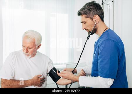 general practitioner will measure the blood pressure on a senior patient. An elderly man suffers from high blood pressure, hypertension Stock Photo