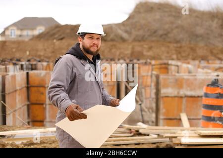 Male caucasian engineer holding drawing plan of hause at construction site. Stock Photo