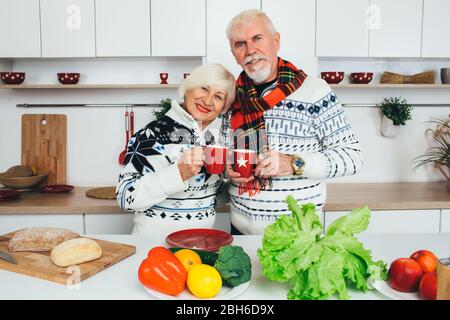 Elderly happy couple drinking tea standing at home in the kitchen, seniors people spending time together at home. Stock Photo