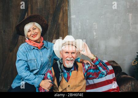 elderly couple dressed in cowboy style, sitting on the couch, looking at each other. Stylish Seniors Stock Photo