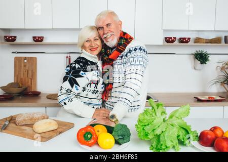 Elderly happy couple, smiling looking at the camera and standing in a beautiful white kitchen. Cooking healthy eating for elderly people Stock Photo