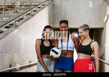 Three multi-ethnic female soccer players at the stadium. Woman soccer team players with a ball at the stadium for training session. Stock Photo