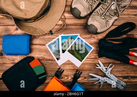 Top view of equipment for hiking and travel on wooden table with photos of nature in the middle. Items include trekking pole, shoes, multi tool, hat, Stock Photo