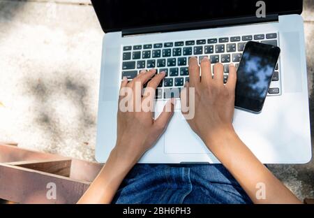 Two hands on the keyboard of computer with the black mobile phone Stock Photo