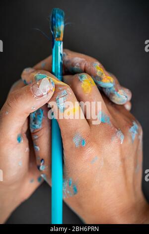 Human hands with paintbrush, stained with paint, artist’s creative process, hobby of a young woman, art and creativity concept Stock Photo