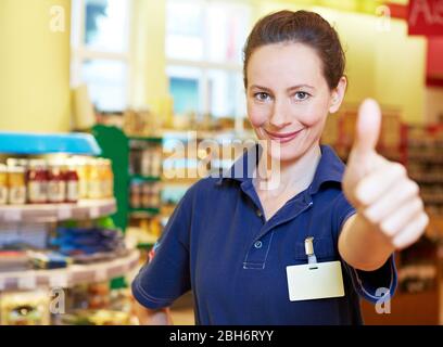 Smiling supermarket saleswoman holds her thumb up Stock Photo