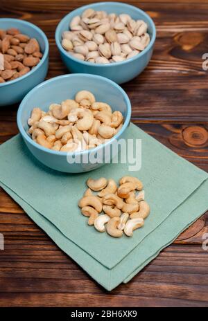 Assorted nuts in dishes on wooden table. Pistachios, cashews, almonds Stock Photo