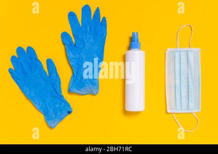 Coronavirus protection. Medical surgical mask, disinfectant or hand sanitizer and blue disposable gloves on yellow background. Hygiene measures to pre Stock Photo