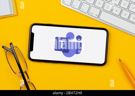 A smartphone showing the Microsoft Teams logo rests on a yellow background along with a keyboard, glasses, pen and book (Editorial use only). Stock Photo