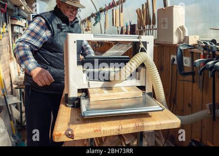Senior craftsman woodworking at carpentry with lots of modern professional power tools. Man using thicknessing planer machine, clamp joiner, circular Stock Photo