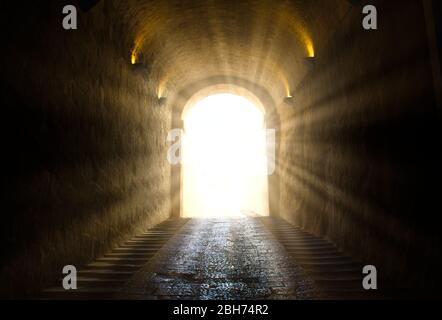 A bright yellow glowing light breaking through at the end of a dark tunnel Stock Photo