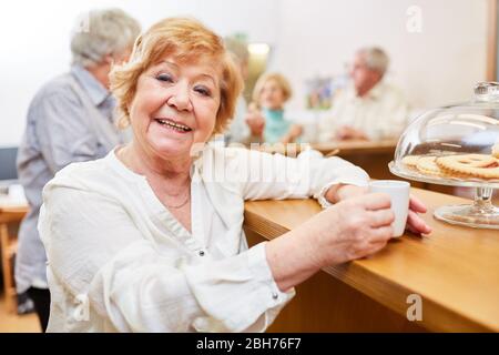 Happy elderly woman drinking espresso in the senior cafe in the retirement home Stock Photo