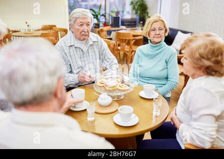 Group of seniors in the retirement home drinking coffee and talking in the common room Stock Photo