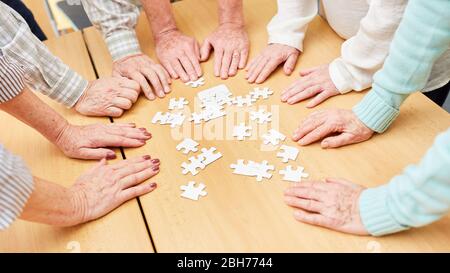 Hands of seniors on a table with puzzle pieces as memory training Stock Photo